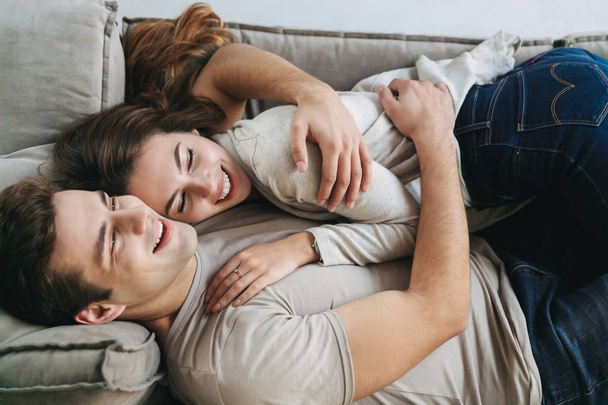 Happy young couple relaxing on a couch at home, embracing - Фото, изображение