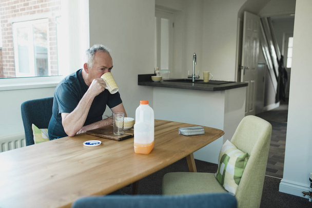 One senior man is sitting at the dining table in his home, enjoying porridge for breakfast with a cup of coffee and a glass of juice.  - Foto, Bild