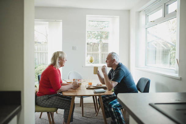Mature couple are having breakfast together at the dining table in their home.  - Fotoğraf, Görsel