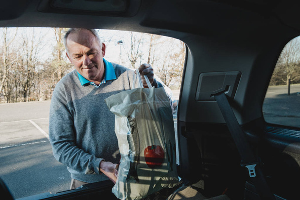 Senior man is placing shopping bags in the boot of his car.  - Valokuva, kuva