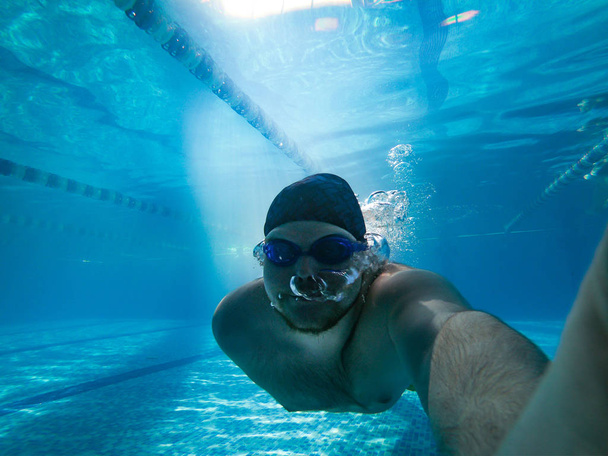 man underwater holding breath in pool. blue goggles - Photo, Image