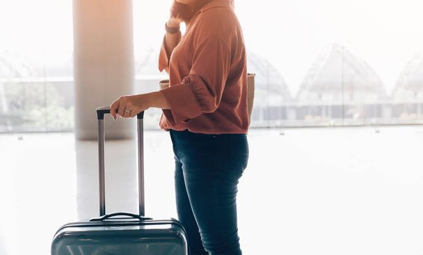 Mujer asiática de pie y sosteniendo la maleta con el check-in de espera para el vuelo en la terminal del aeropuerto
. - Foto, imagen
