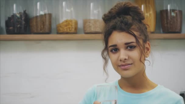 Gorgeous, beautiful, young woman holding glass of fresh water and smiling while standing in kitchen in the morning - Filmagem, Vídeo