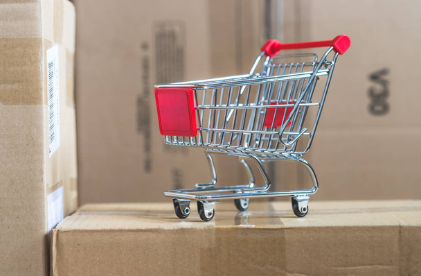 Online-Shopping and parcel service concept: Miniature shopping cart and cardboard boxes - 写真・画像