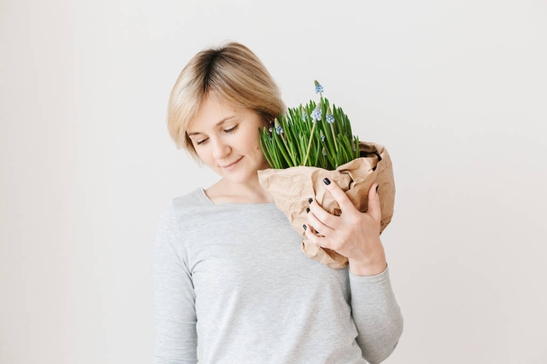 Portrait of middle aged woman on light background. Mother holding potted spring flowers muscari gift. Mothers day concept - Fotoğraf, Görsel