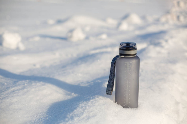 Grey spotive plastic drink bottle in snow. - Foto, afbeelding