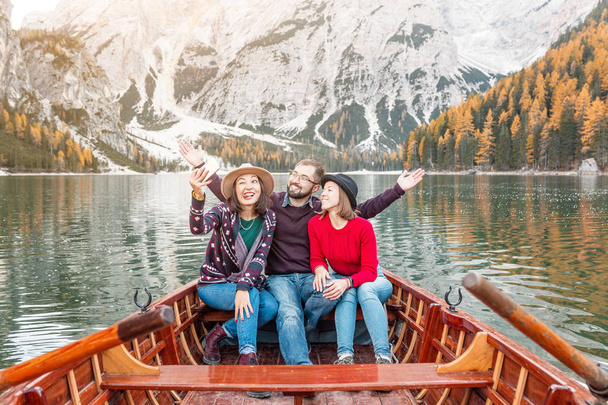 Csoport három boldog utazók egy fából készült hajón, a tó a hegyek között. Pihenés és a turizmus az olasz Dolomitok koncepció - Fotó, kép
