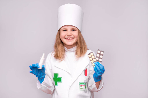 Usměvavá holčička v lékařských uniformě Držte nosní sprej a pilulky pro zdraví. Lékař doporučuje lék sprej - Fotografie, Obrázek