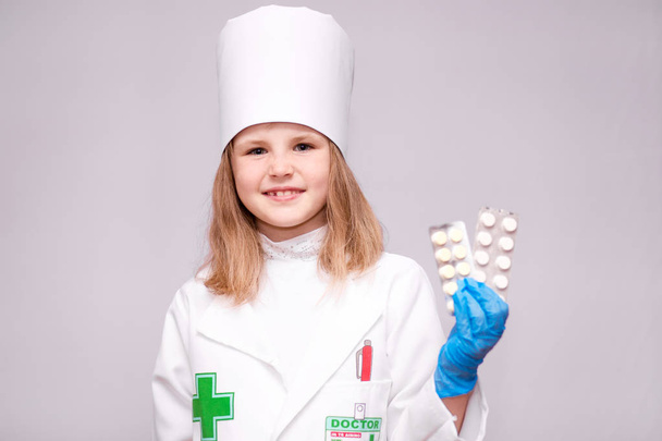 Niña sonriente con uniforme médico sosteniendo pastillas para la salud. El médico recomienda pastillas para medicamentos
 - Foto, Imagen