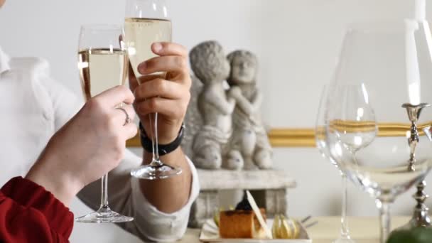 Concept van romantische relaties. Handen met champagne in glazen. Close-up shot van jong koppel op een dating dineren in een restaurant. Twee glazen in handen met mooie engelen beeldje op de achtergrond. HD - Video