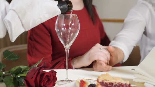 Una foto mediana de una joven pareja de manos en la mesa. Moción lenta de camarero vertiendo champán a pareja amante de tener una cena romántica en el restaurante. Concepto romántico
. - Metraje, vídeo