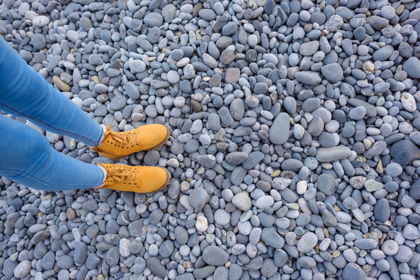 Felsstrand. Kieselsteine. runde Steine in verschiedenen Größen. Schwarzes Meer. Massandra Strand. yalta. Ruhe auf der Krim. Spaziergang am Strand entlang. Füße in gelben Schuhen. - Foto, Bild