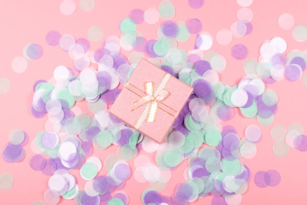 色とりどりの紙吹雪とピンクの背景に光沢のあるサテンの弓と小さなかわいいプレゼント ボックス。フラット レイアウト スタイルです。休日および祭典のコンセプト. - 写真・画像