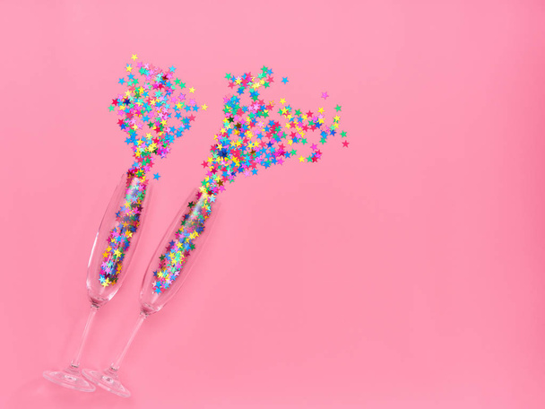 Two champagne glasses with colorful confetti  on pink  background. Flat lay, top view celebrate party concept - Photo, Image