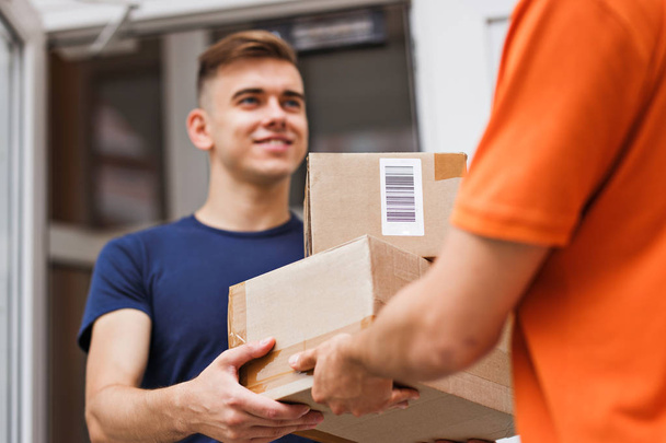 A person wearing an orange T-shirt is delivering parcels to a satisfied client. Friendly worker, high quality delivery service. - Valokuva, kuva