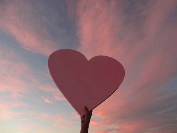 Nainen käsi tilalla iso vaaleanpunainen sydän taustalla vaaleanpunainen
 - Valokuva, kuva