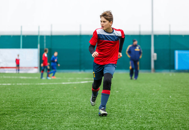 Boys in red white sportswear running on soccer field. Young footballers dribble and kick football ball in game. Training, active lifestyle, sport, children activity concept  - Photo, Image