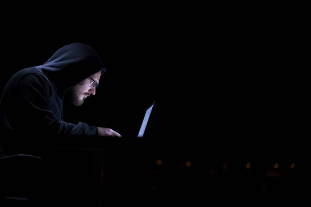 Young talented hacker using laptop computer while working in dark office with big city lights in the background at night - Foto, Imagem