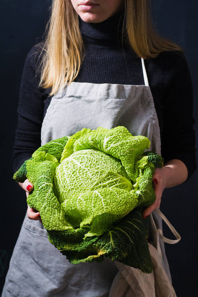 The chef is holding Savoy cabbage. Dark background, side view - Photo, Image