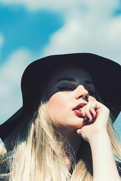 Beauty and fashion look in vintage style. Girl on sunny blue sky background in summer. Fashion woman model pose outdoor. Makeup on young face. Pretty girl in black elegant retro hat and red lips - Zdjęcie, obraz