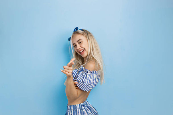 Joyful and excited beautiful blonde girl in summer outfit, pointing at camera, standing over blue background - Fotoğraf, Görsel