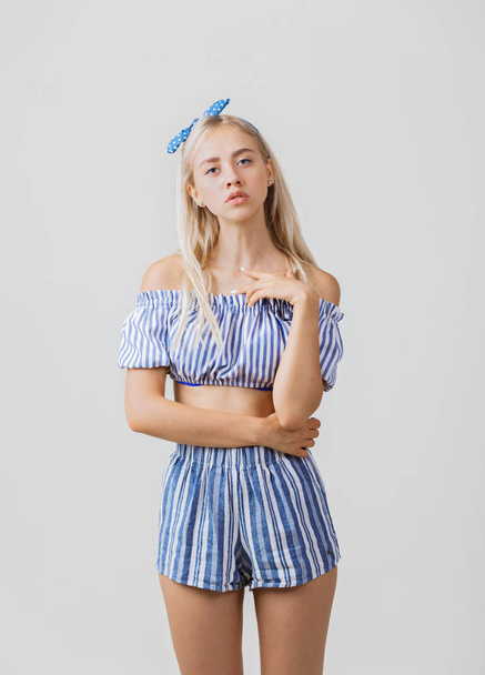 Calm and thoughtful beautiful blonde girl in summer outfit is standing, over white background. Emotions, gestures and facial expression - Fotó, kép