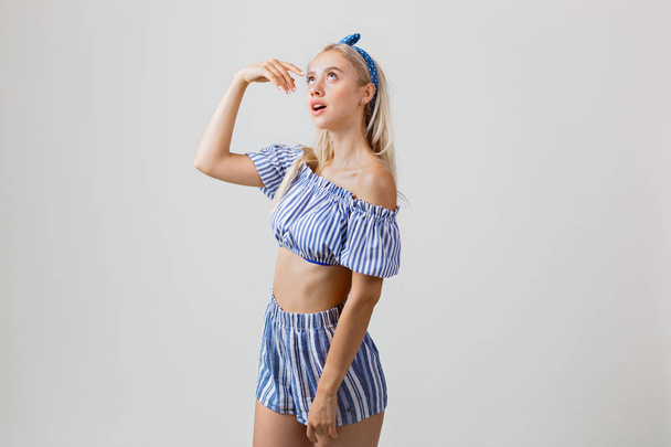 Joyful beautiful blonde girl in summer outfit is looking up with dreamy facial expression, over white background. Emotions, gestures and facial expression - Foto, Bild