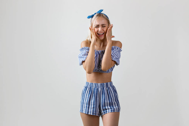 Joyful and super excited beautiful blonde girl in summer outfit, smiling and laughing standing over white background - 写真・画像