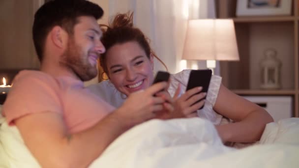happy couple using smartphones in bed at night - Záběry, video