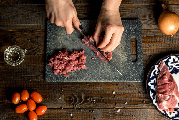 готувати руки нарізати червоне м'ясо на дошці. Поруч помідори, цибуля, масло. Горизонтальна рамка
 - Фото, зображення