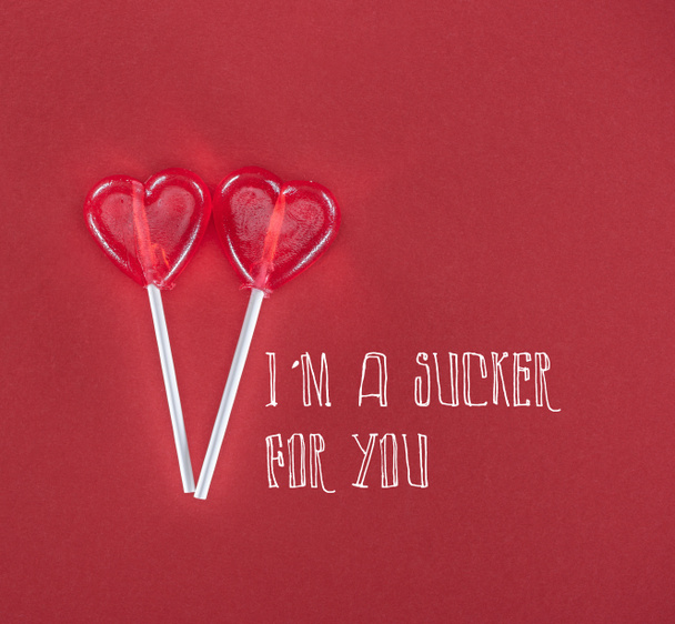 two heart shaped lollipops on red background with "I am a sucker for you" lettering, valentines day concept  - Valokuva, kuva