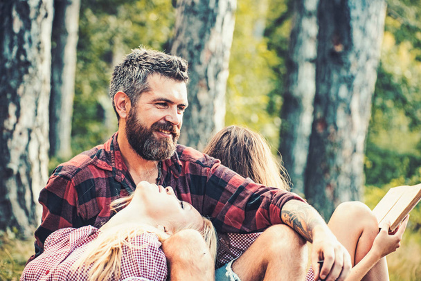Couple in love enjoying warm summer day in forest, romantic weekend together. Blond girl looking at bearded man with affection. Happy friends having picnic in forest - Фото, изображение