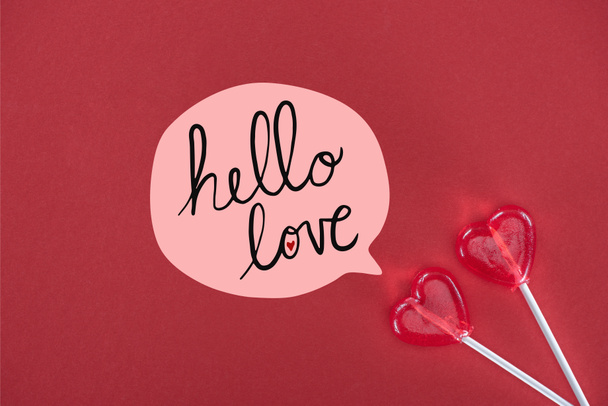 vue du haut de deux sucettes en forme de coeur sur fond rouge avec lettrage "bonjour amour", concept de Saint-Valentin
  - Photo, image