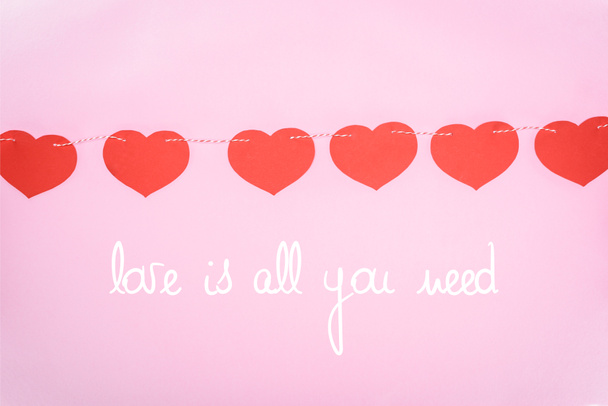 hermosos corazones rojos decorativos colgando de la cuerda en el fondo rosa con letras "El amor es todo lo que necesitas", concepto de día de San Valentín
 - Foto, imagen