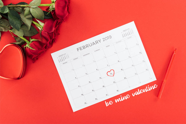 top view of roses and calendar with 14th february date marked with heart isolated on red, st valentines day concept with "be mine valentine" lettering - Foto, Imagem