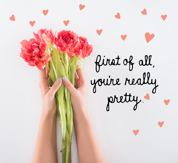 cropped view of woman holding tulips in hands isolated on white with "first of all, you are really pretty" lettering - Фото, изображение