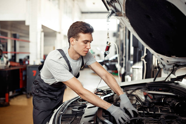 A good-loking young mechanic is reparing a vehicle at his work - Foto, Imagem