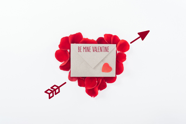 top view of envelope with "be mine valentine" lettering and heart made of red rose petals isolated on white, st valentines day concept - Photo, Image
