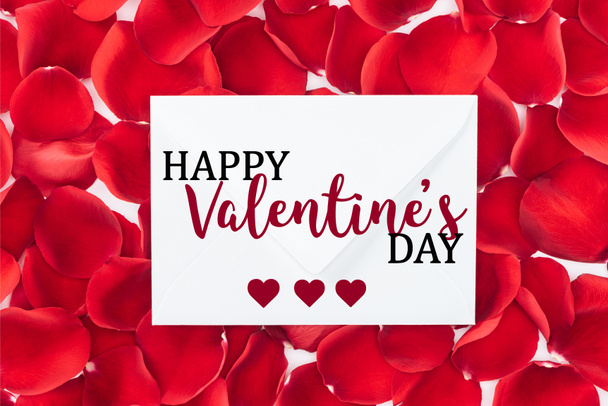 Draufsicht auf Umschlag mit "Happy Valentines Day" -Schriftzug und roten Rosenblättern auf Hintergrund - Foto, Bild