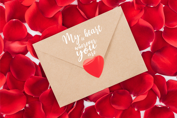 top view of envelope with "my heart is wherever you are" lettering, heart and red rose petals on background, st valentines day concept - Photo, Image