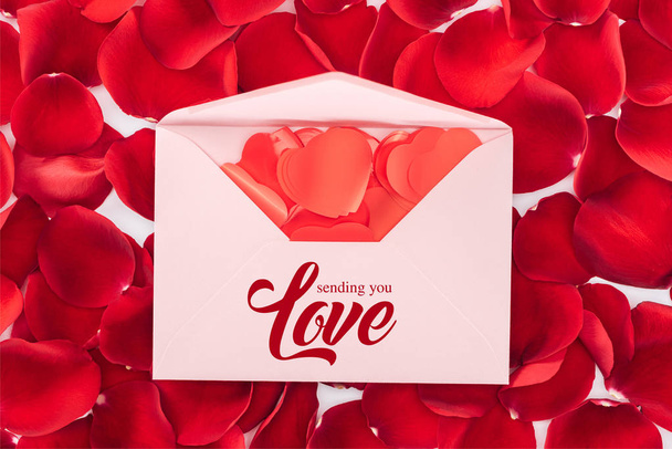 top view of envelope with "sending you love" lettering, heart shaped confetti and red rose petals on background, st valentines day concept - Photo, Image