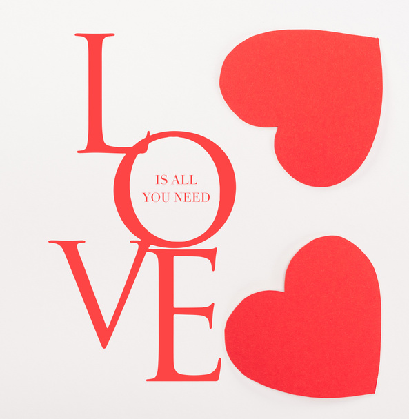 Draufsicht auf rote, herzförmige Papierkarten auf weißem Papier mit dem Schriftzug "Liebe ist alles, was man braucht", Valentinstag-Konzept - Foto, Bild
