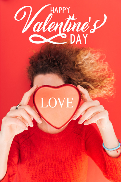 top view of girl holding heart symbol with "love" lettering in front of face isolated on red, happy valentines day concept - Foto, afbeelding