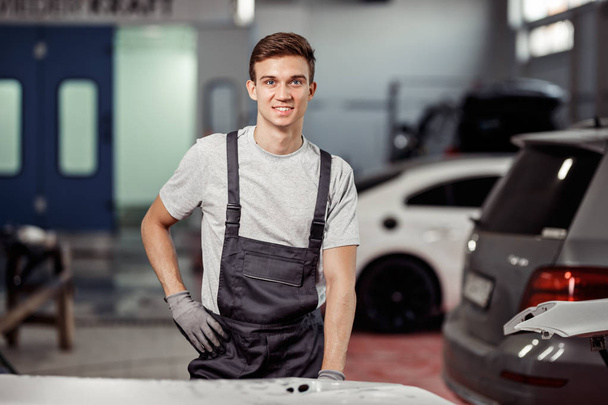 A yound car mechanic is leaning upon a white car at a car service - Fotoğraf, Görsel