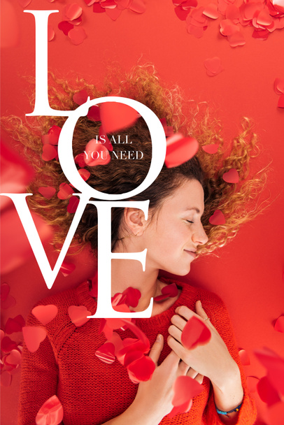 bovenaanzicht van het meisje en dalende hart vormige confetti geïsoleerd op rood met "Love is alles wat u nodig hebt" belettering, st Valentijnsdag concept - Foto, afbeelding