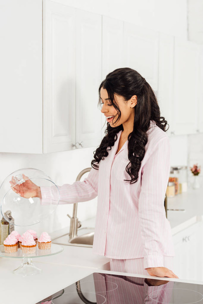 belle afro-américaine fille tenant dôme de cupcakes sur support en verre dans la cuisine
 - Photo, image