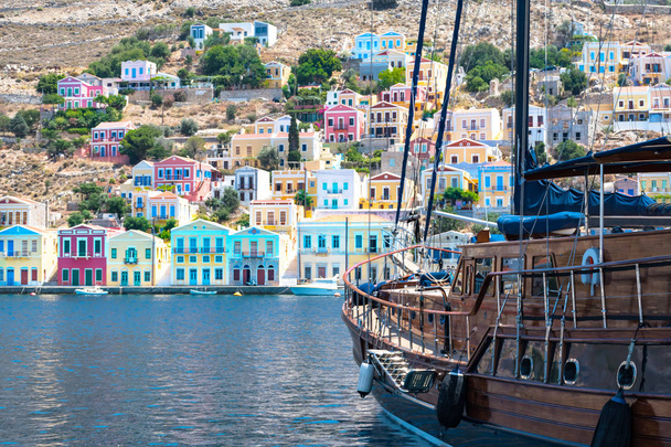 Grote zeilboot en kleurrijke neoklassieke huizen in haven stad van Symi (Simi Island, Griekenland) - Foto, afbeelding