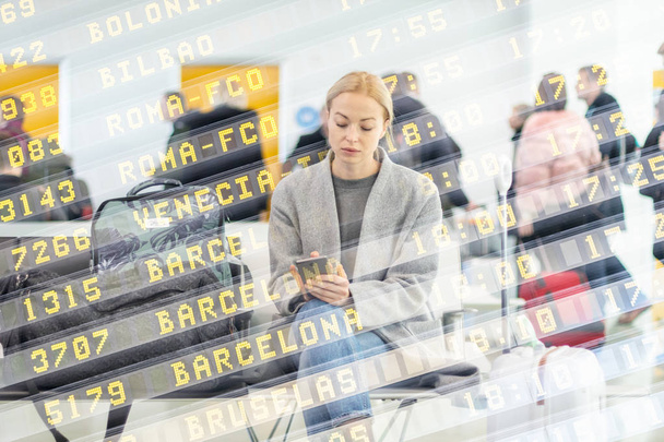 Женщина-путешественница использует свой мобильный телефон в ожидании посадки на самолет на выходе из терминала аэропорта
. - Фото, изображение