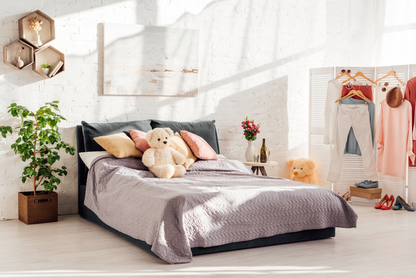 modern interior design of bedroom with teddy bear toys, pillows, clothes on racks and bed - Foto, immagini