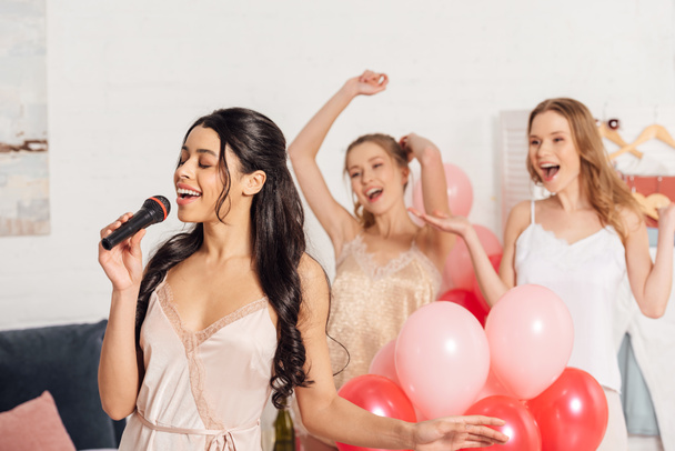 beautiful multiethnic girls in nightwear singing karaoke at pajama party in bedroom - Foto, Imagem